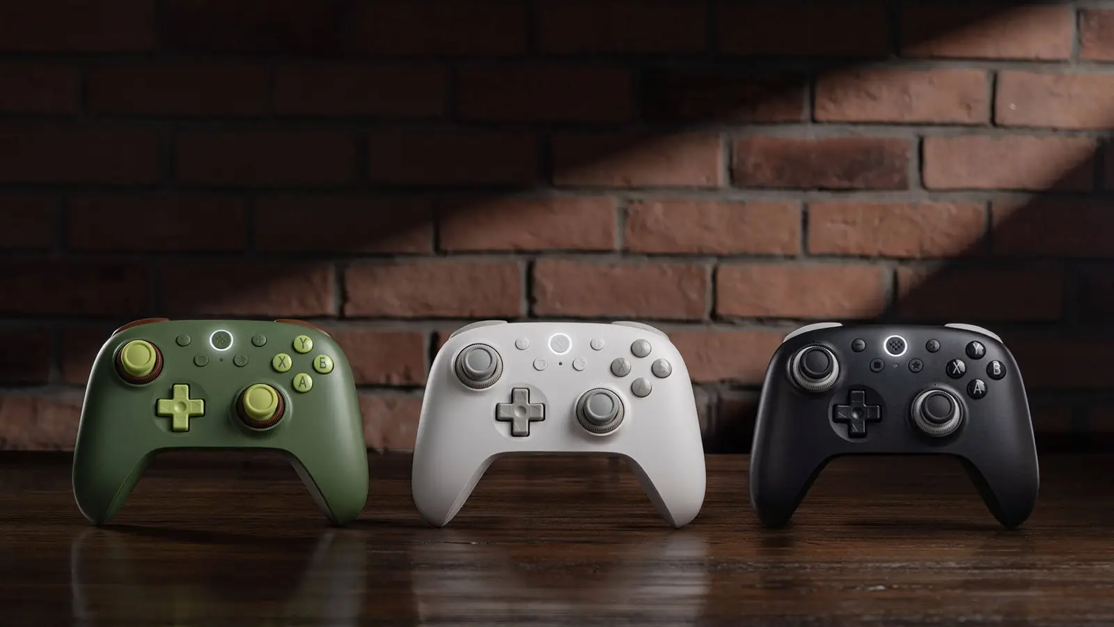 Three 8BitDo Ultimate 3C+ controllers, in avocado green, frost white and stealth black, standing side by side on a wooden shelf in front of a brick wall.