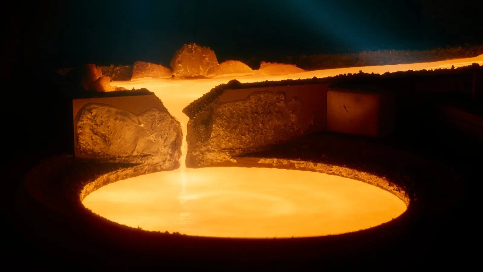 Glowing orange molten titanium pouring into a round vessel inside a dark foundry.