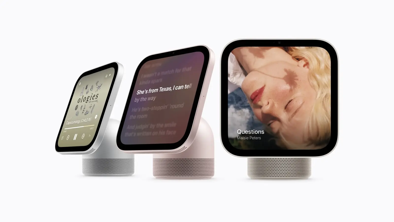Three HomeView displays on speaker bases in silver, pink and starlight, showing a music player, scrolling song lyrics and album art on a light background.