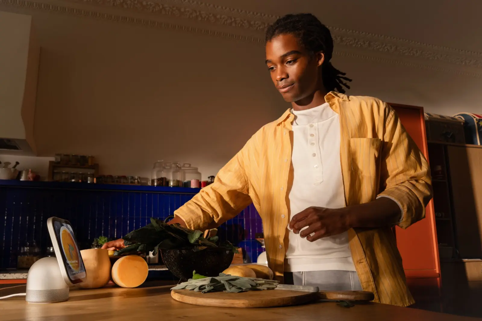 A person in a yellow shirt prepares vegetables at a kitchen counter, with a HomeView on a speaker base at the left edge of the counter.