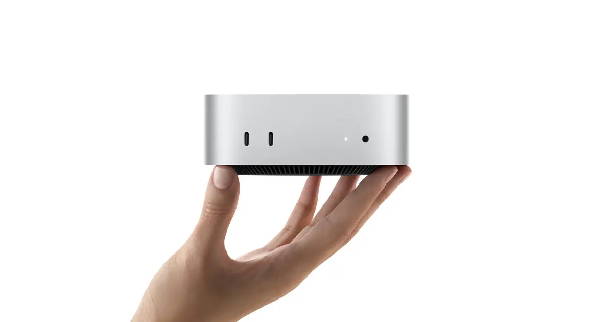 Apple's silver Mac mini resting on a human hand against a white background, with its front ports visible.