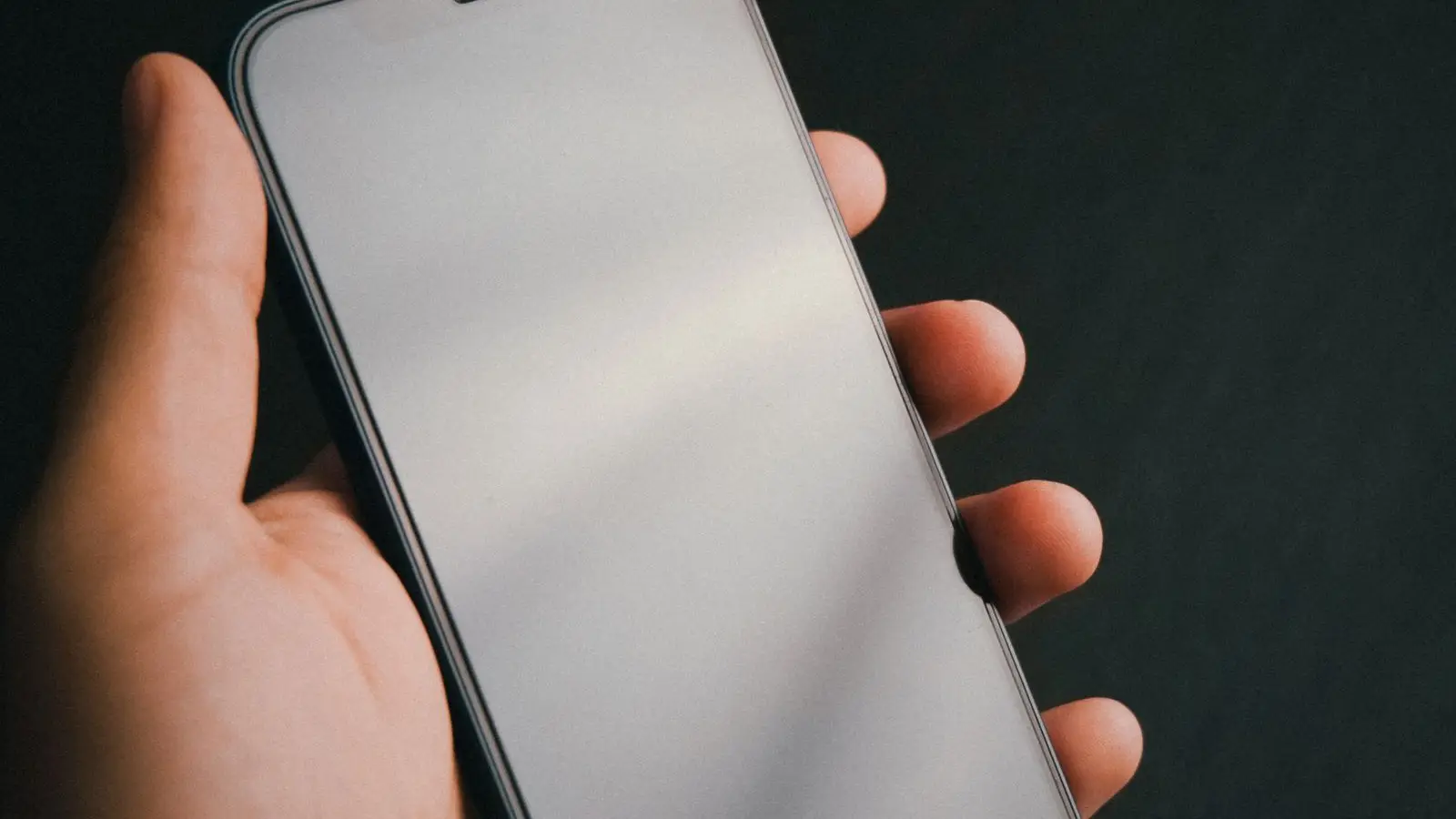 A hand holding a smartphone with a blank screen against a dark background