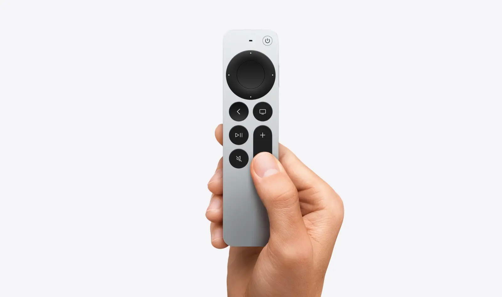 A hand holding the silver and black Siri Remote with its clickpad, back, TV, play, mute and volume buttons.