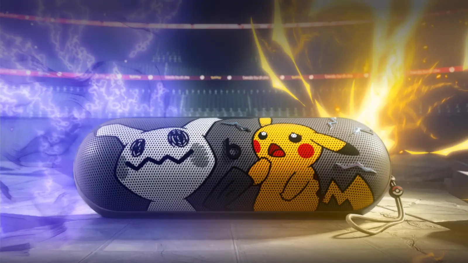 The special-edition Pokémon Beats Pill speaker lying on a stone floor in a stadium, with Mimikyu on the left of the grill, Pikachu on the right and a carry lanyard with a Poké Ball charm at the right end.