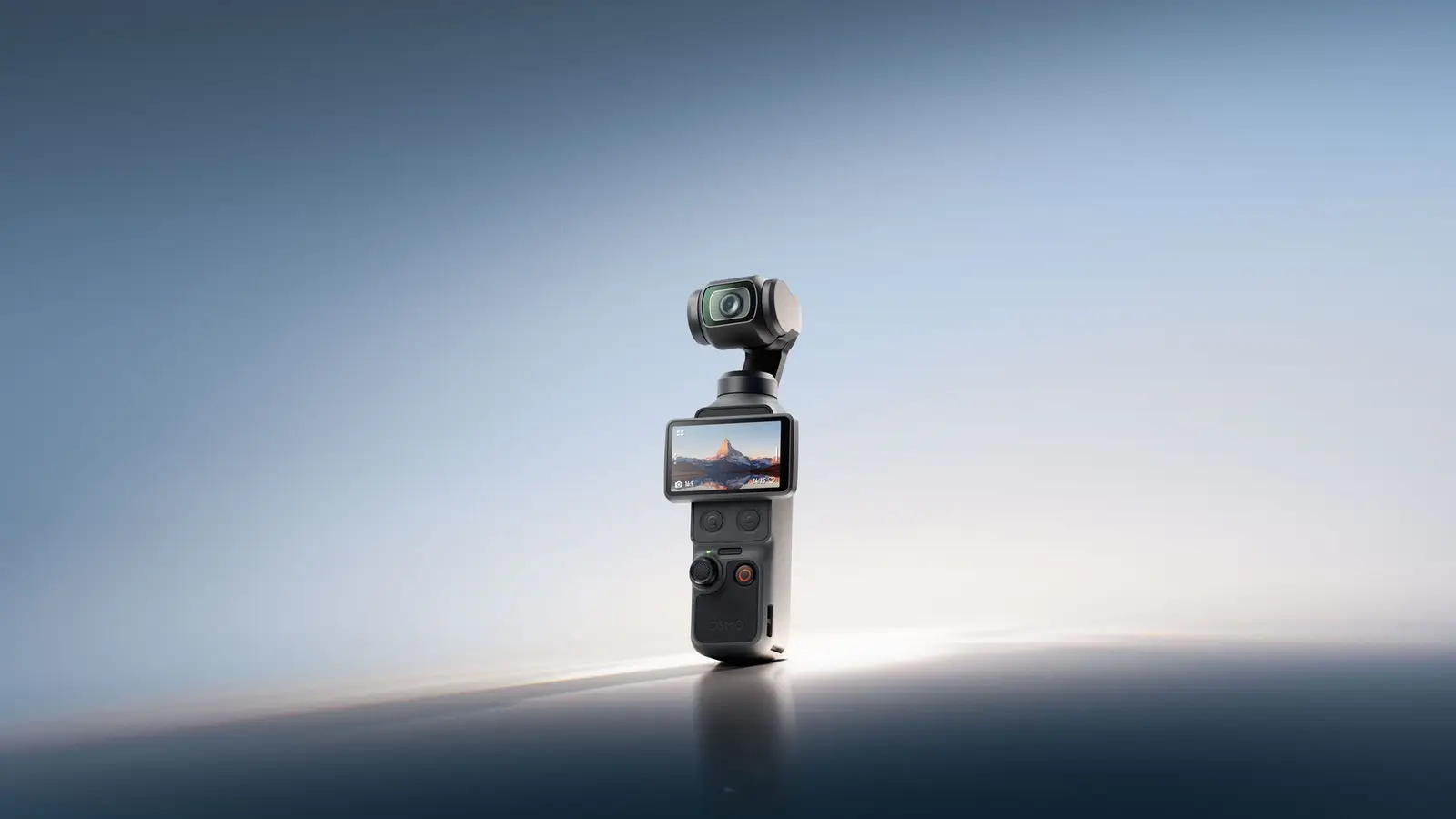 A DJI Osmo Pocket 4 standing upright on a dark reflective surface against a pale blue gradient, its screen showing a mountain photo.