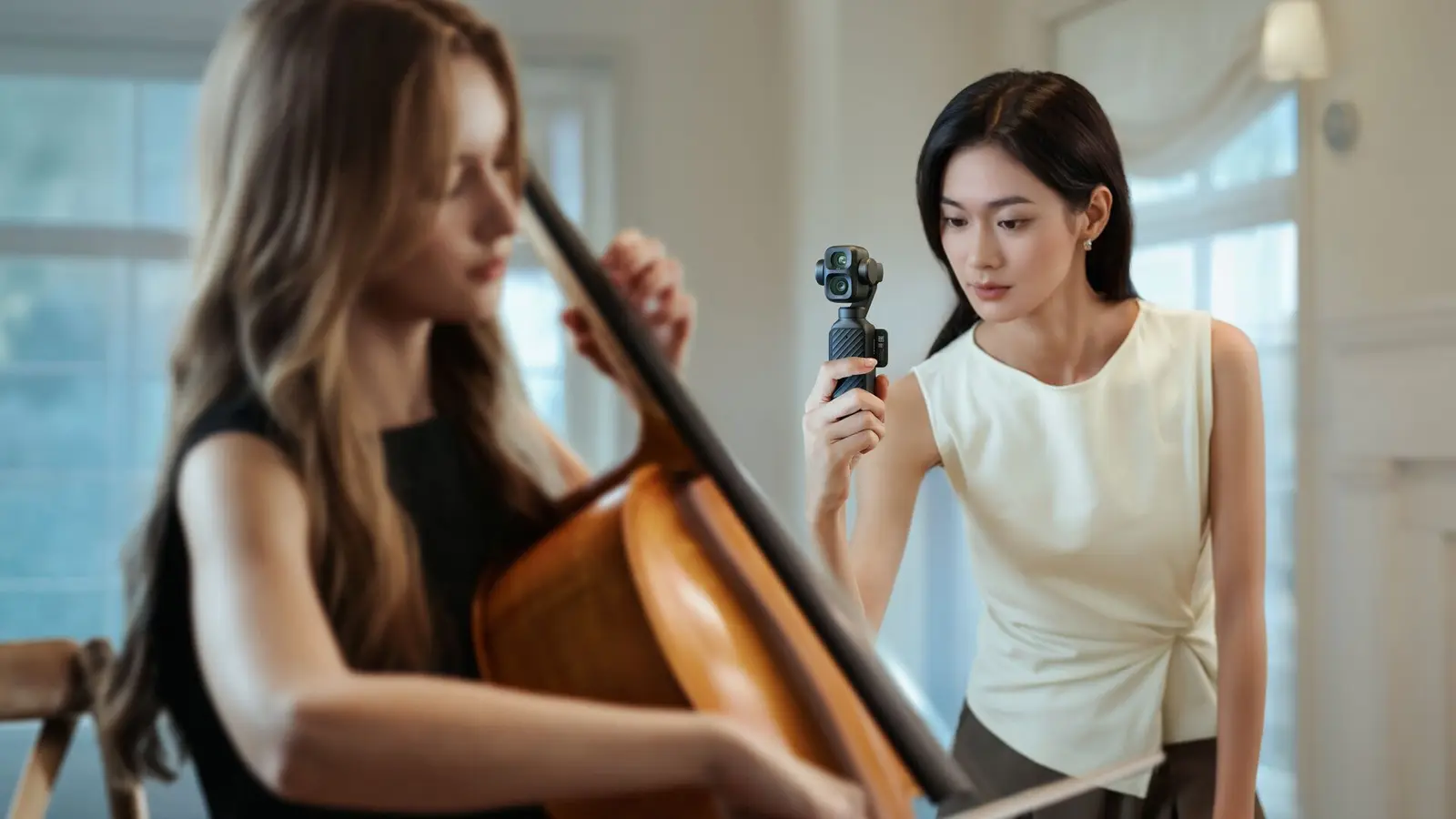 A woman holds a black DJI Osmo Pocket 4P with two lenses at eye level while a woman in the foreground plays a cello.