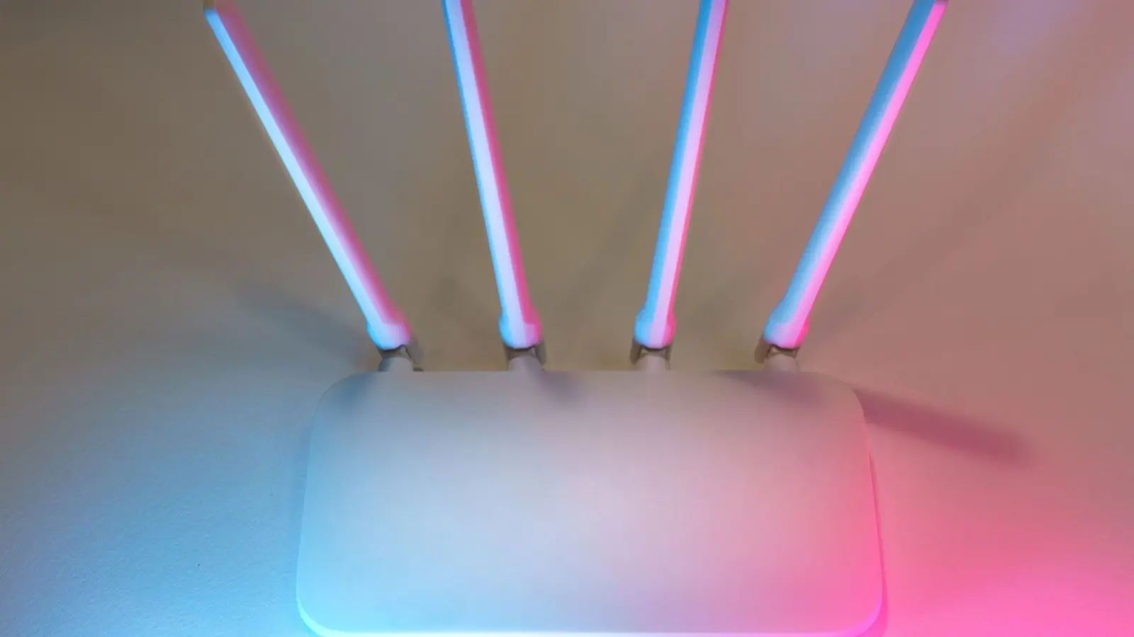 A white four-antenna wireless router lit in blue and pink, seen from above against a pale wall.