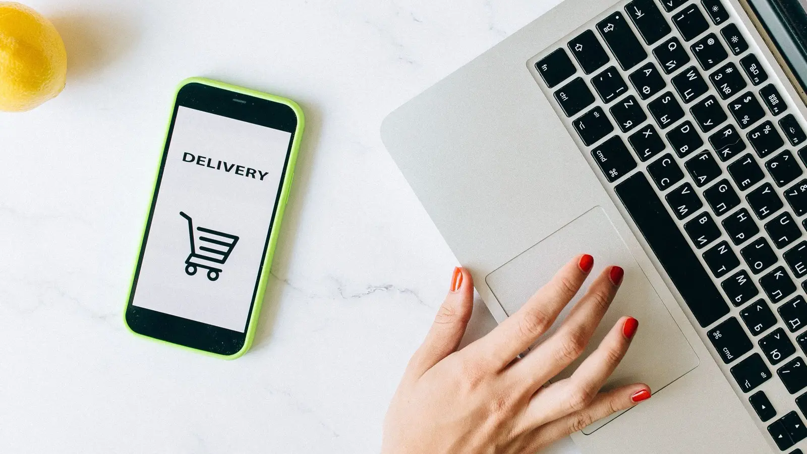 A phone showing the word Delivery and a shopping cart icon next to a laptop and a hand on its trackpad.