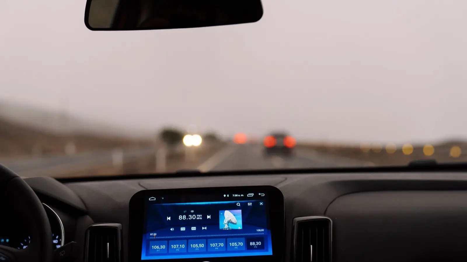 View through a car windshield on a foggy road, with an infotainment screen showing a radio on the dashboard
