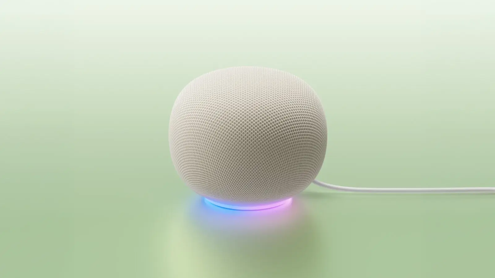 A white fabric-covered Google Home Speaker with a blue and pink light ring, on a pale green surface.