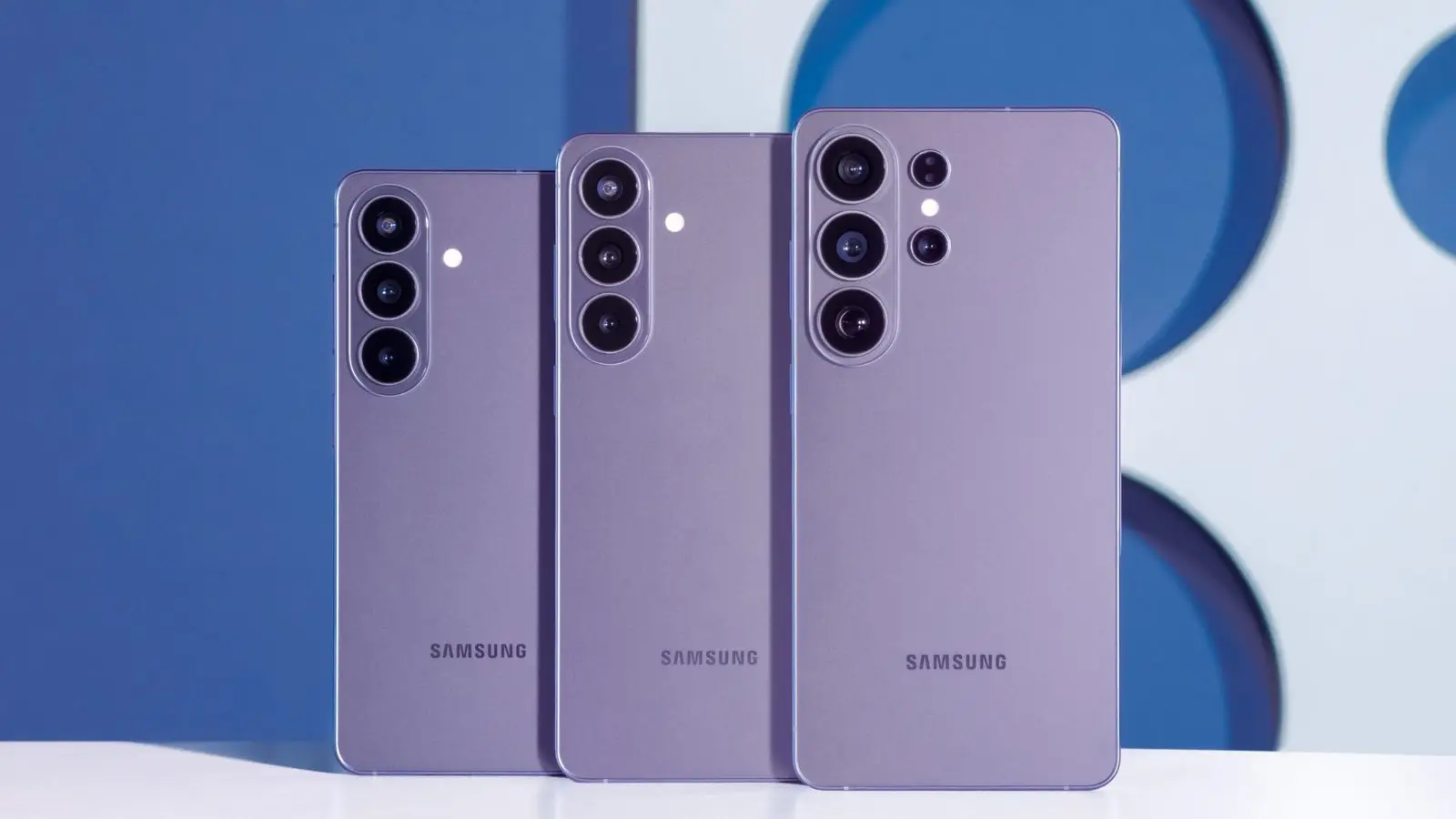 Three purple Samsung Galaxy S26 series phones standing back-first against a blue backdrop, showing their camera modules.