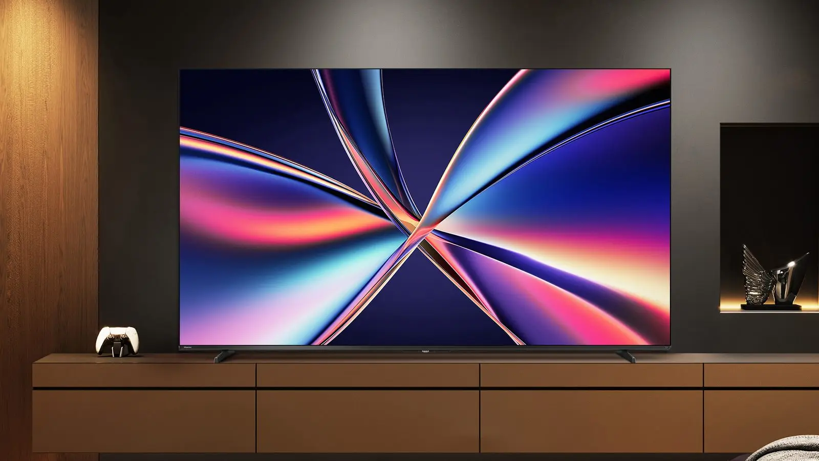 A Hisense E6 Series TV on a media console in a dark living room, its screen showing swirling blue, pink and orange ribbons, with a game controller beside it.