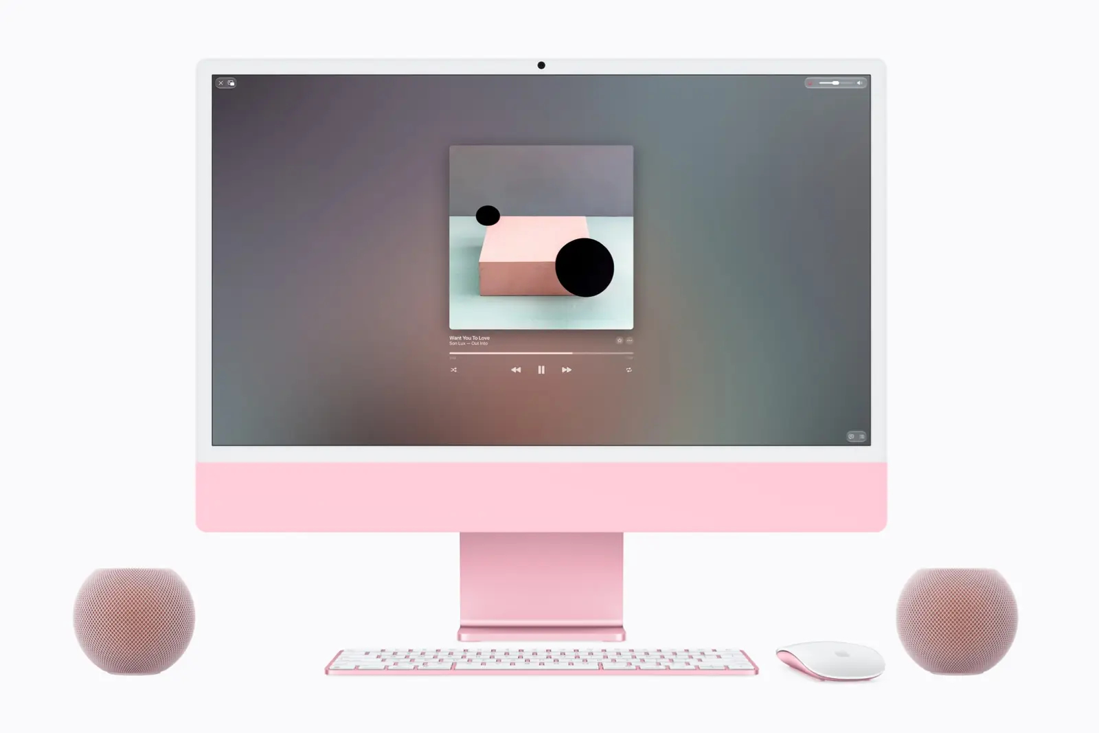 A pink iMac playing music, with a pink HomePod mini 2 on each side of its stand, beside a pink keyboard and mouse.