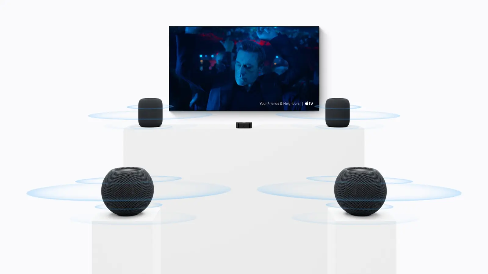 A wall-mounted TV with an Apple TV 4K box below it. Two tall HomePod speakers stand on a plinth at the front and two round HomePod mini 2 speakers sit on plinths in the foreground, each ringed by blue sound waves.