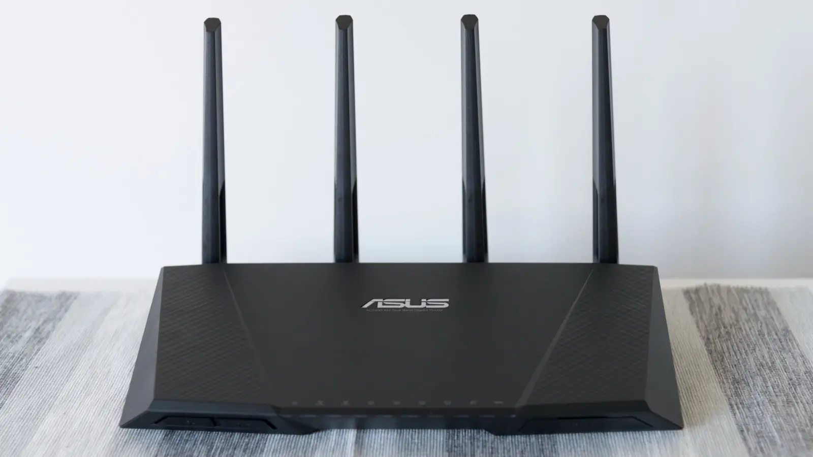 A black ASUS Wi-Fi router with four upright antennas, seen from the front on a table.