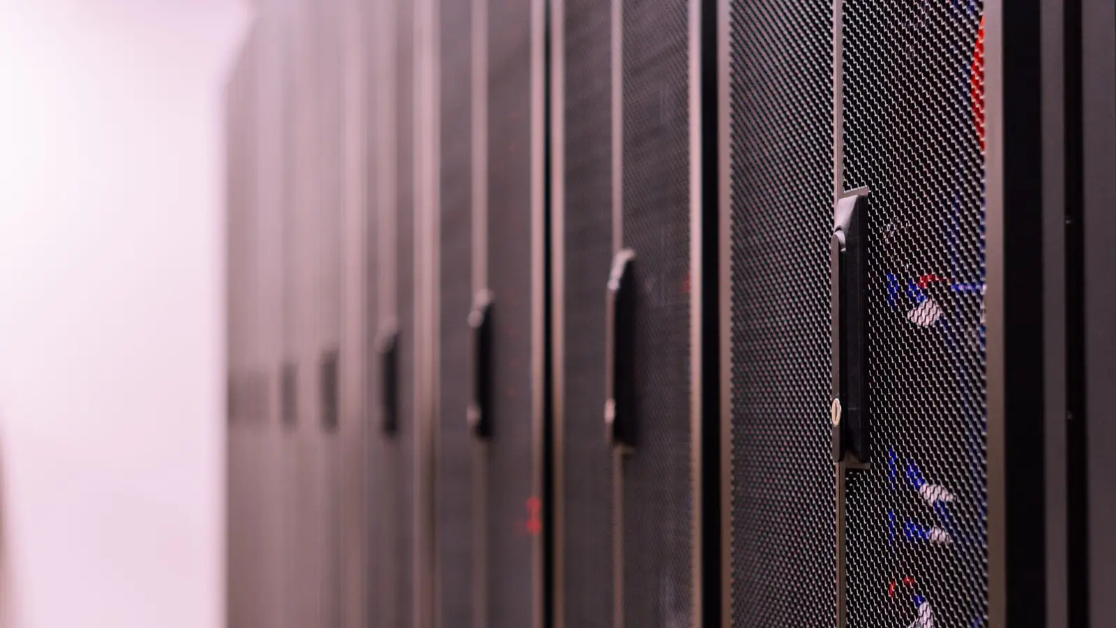 A row of black mesh-door server cabinets in a data center, in soft focus.