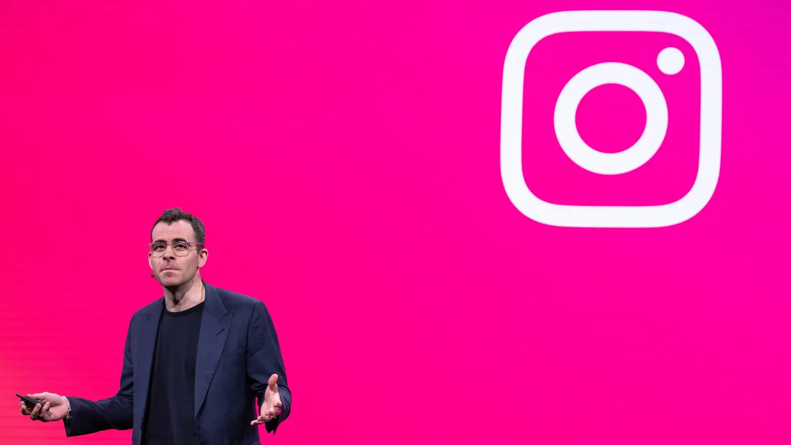 Instagram head Adam Mosseri speaking on stage in front of a bright pink screen showing the Instagram logo.