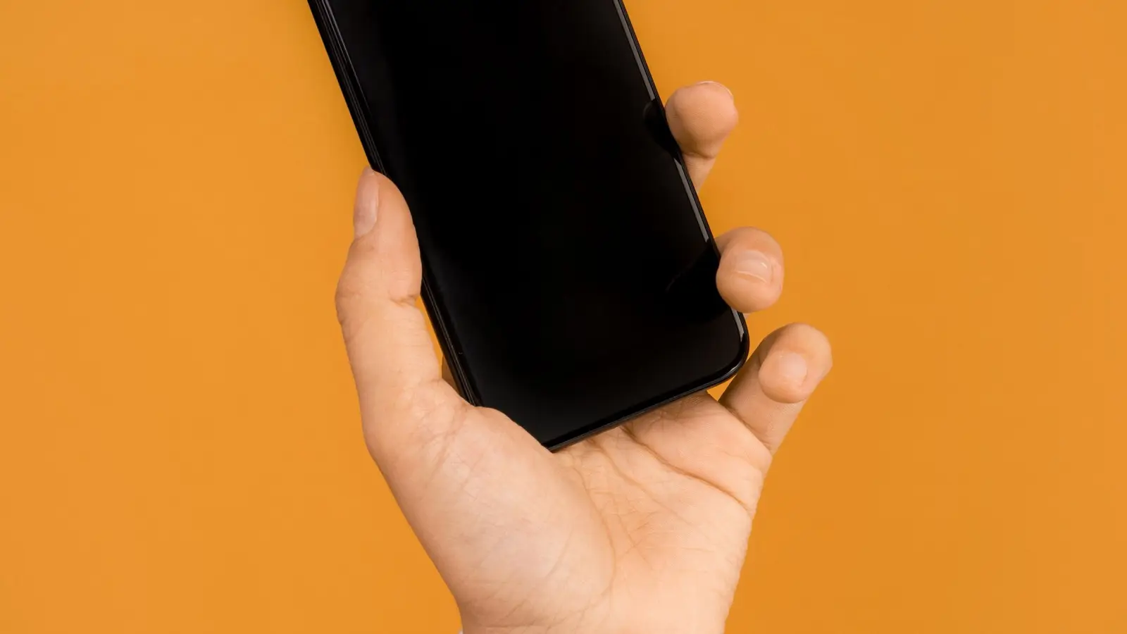 A hand holding a black smartphone against an orange background.