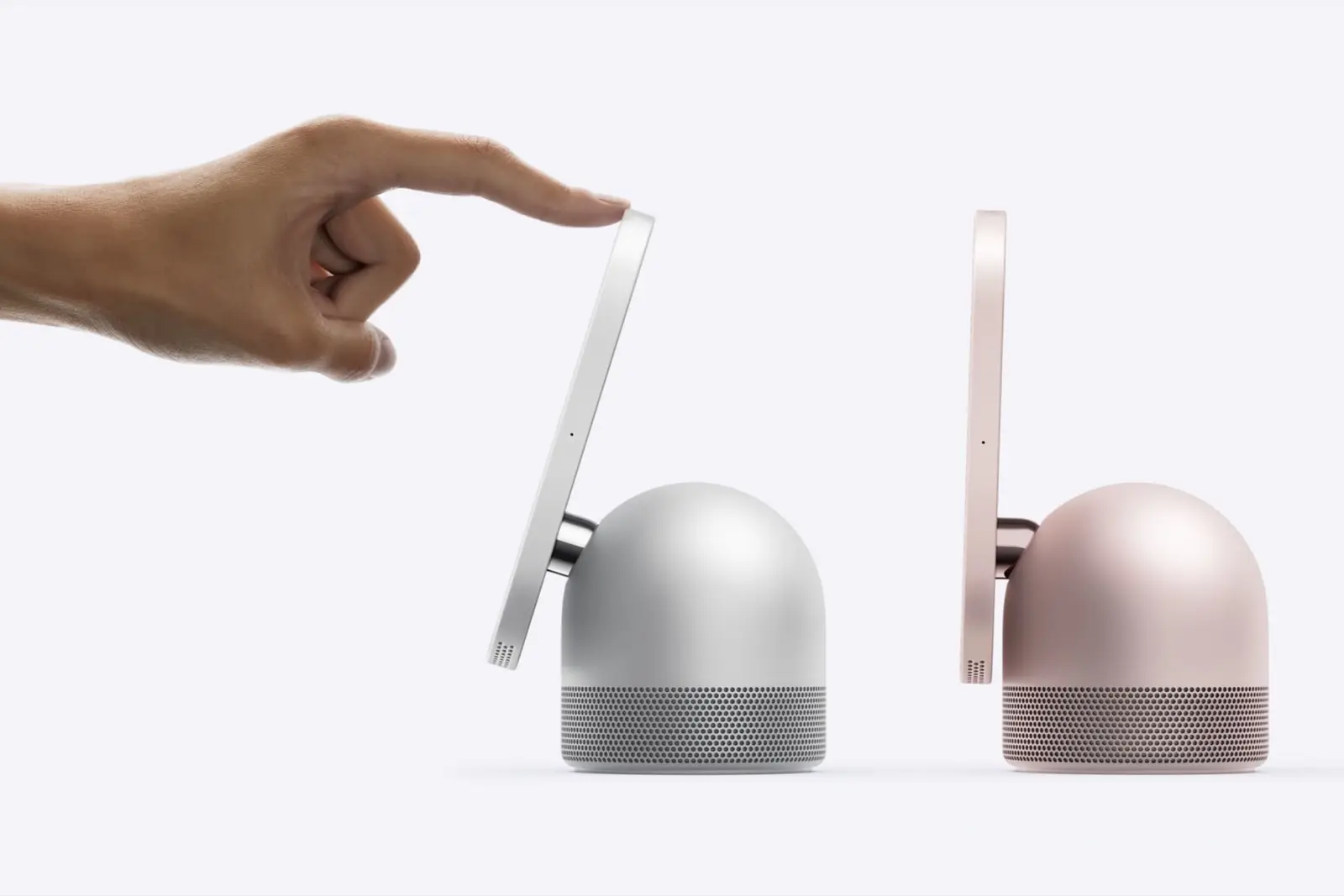 Two HomeView displays seen from the side on domed speaker bases, one silver and one rose pink, with a hand tilting the silver screen.