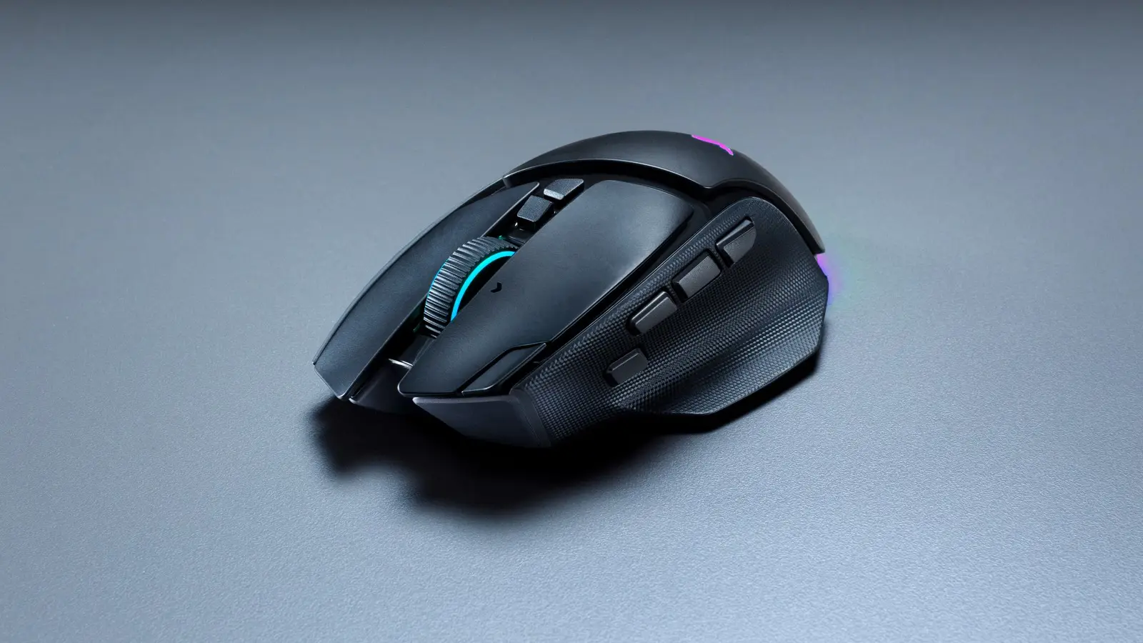 Black Razer Basilisk V4 Pro seen three-quarter from above on a grey surface, with its scroll wheel lit cyan.