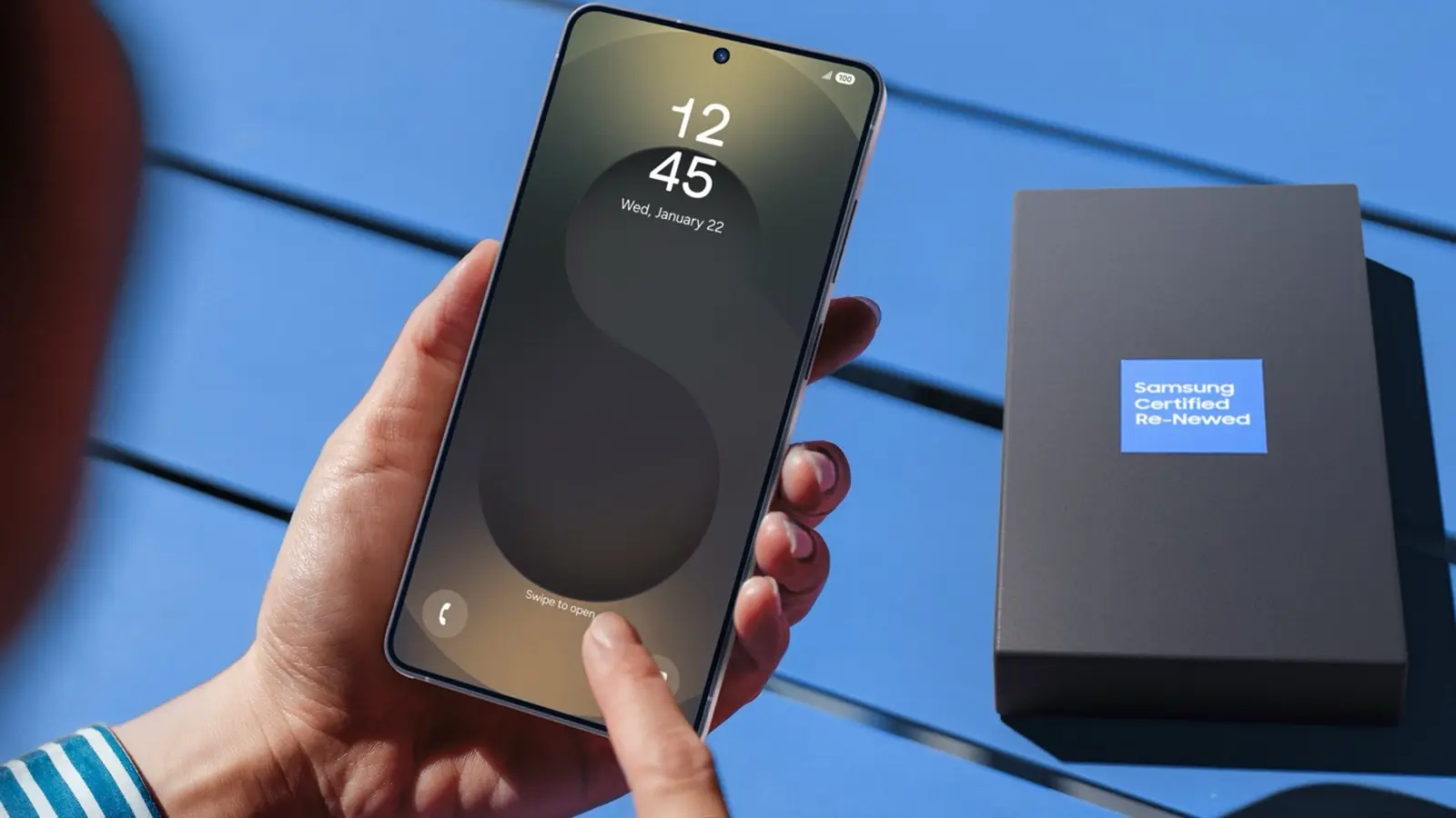 A hand holding a Galaxy phone next to a Samsung Certified Re-Newed box.