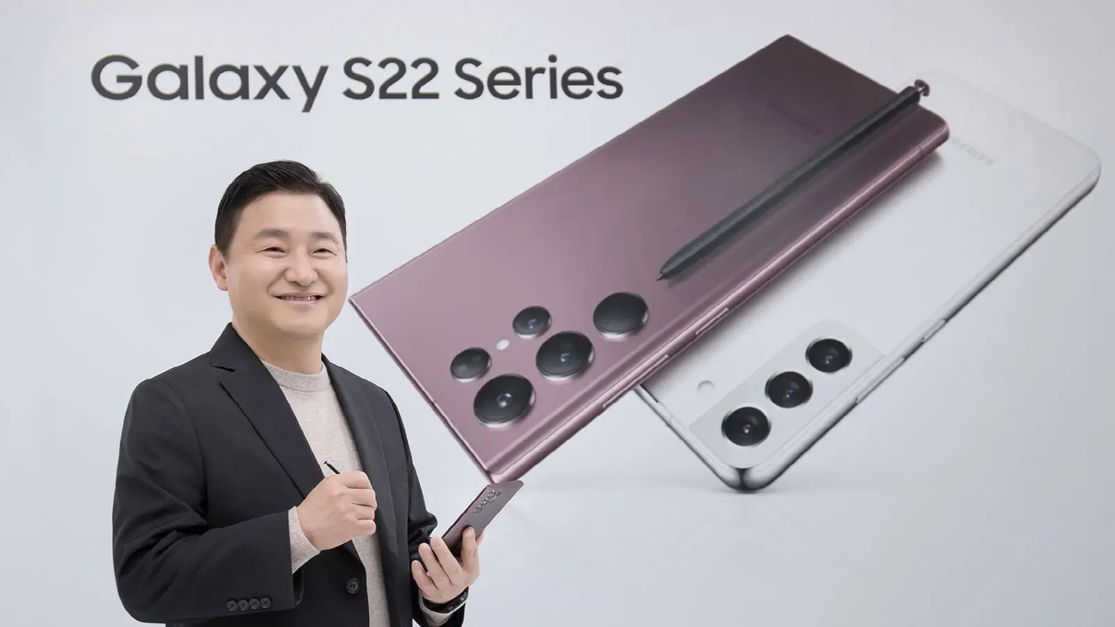 A Samsung presenter holds a Galaxy S22 Ultra and S Pen in front of Galaxy S22 series artwork.