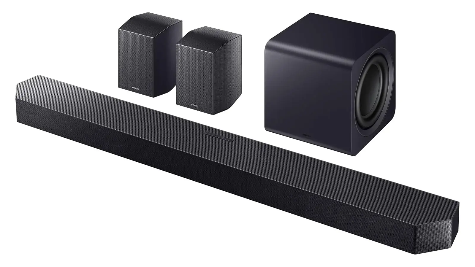 A dark grey Samsung soundbar seen at an angle, with two small rear speakers and a cube-shaped wireless subwoofer behind it, on a white background.