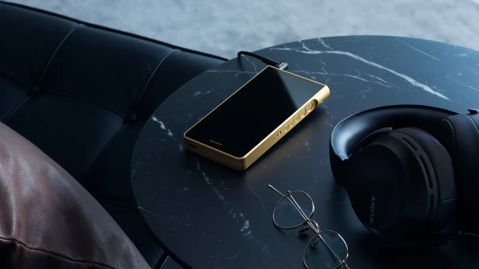 Gold NW-WM1ZM3 Walkman on a black marble table beside Sony headphones and a pair of round glasses.