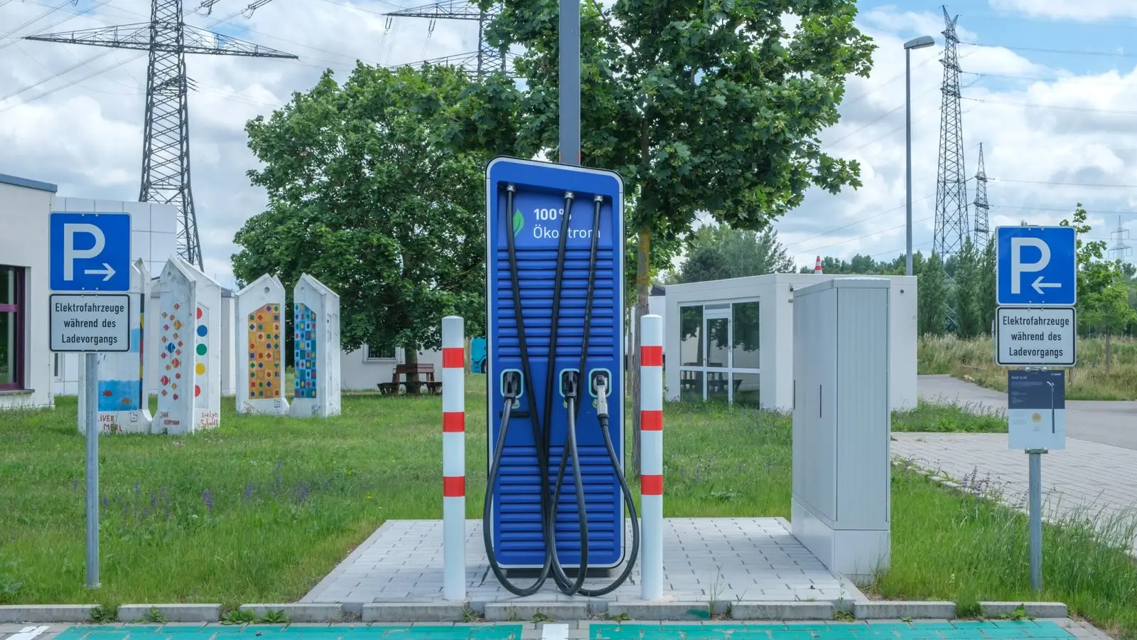 A blue public fast charger for electric vehicles on a grass lot, with parking signs on either side.