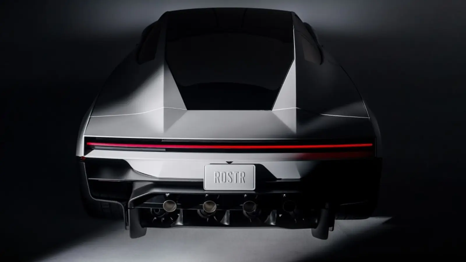 Rear view of a silver Tesla Roadster in a dark studio, with a red light bar and a plate reading RDSTR.